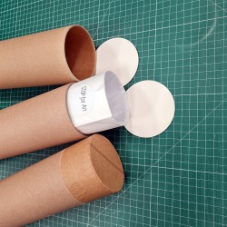 Podłożem zdjęcia jest mata introligatorska, na której znajdują się trzy tuby kartonowe w różnych fazach pakowania wydruku. Od góry tuba pusta z papierowym denkiem, po środku tuba z wystającym plakatem zawiniętym w pergamin i nakleją z logo sklepu, na spodzie tuba zamknięta papierowym denkiem i zabezpieczona taśmą papierową 